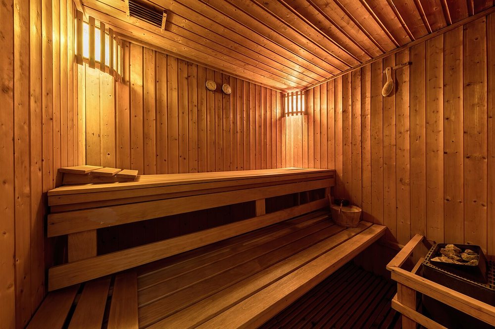A wood-lined sauna with tiered benches, warm wall lights and a heater with stones